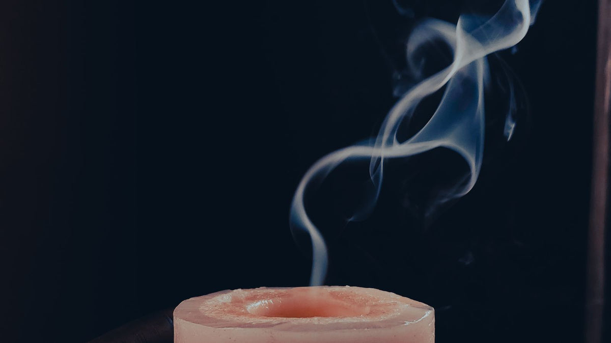 Smoke rising from a pink pillar candle against a dark background
