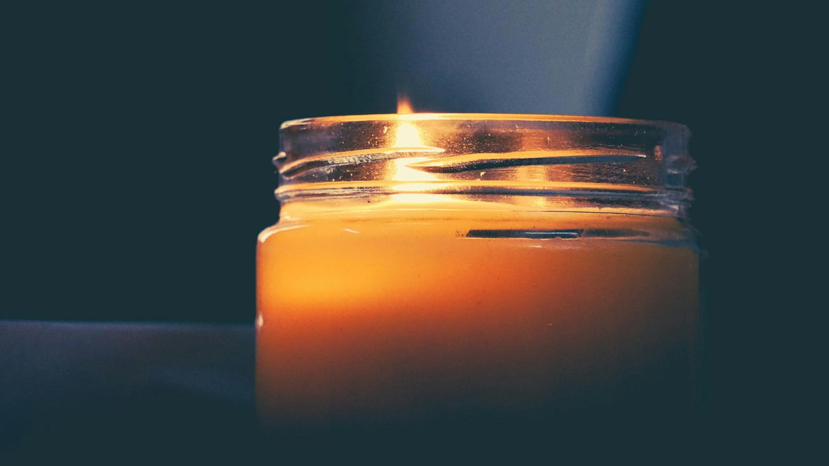 A lit candle in a clear glass jar against a dark blue background