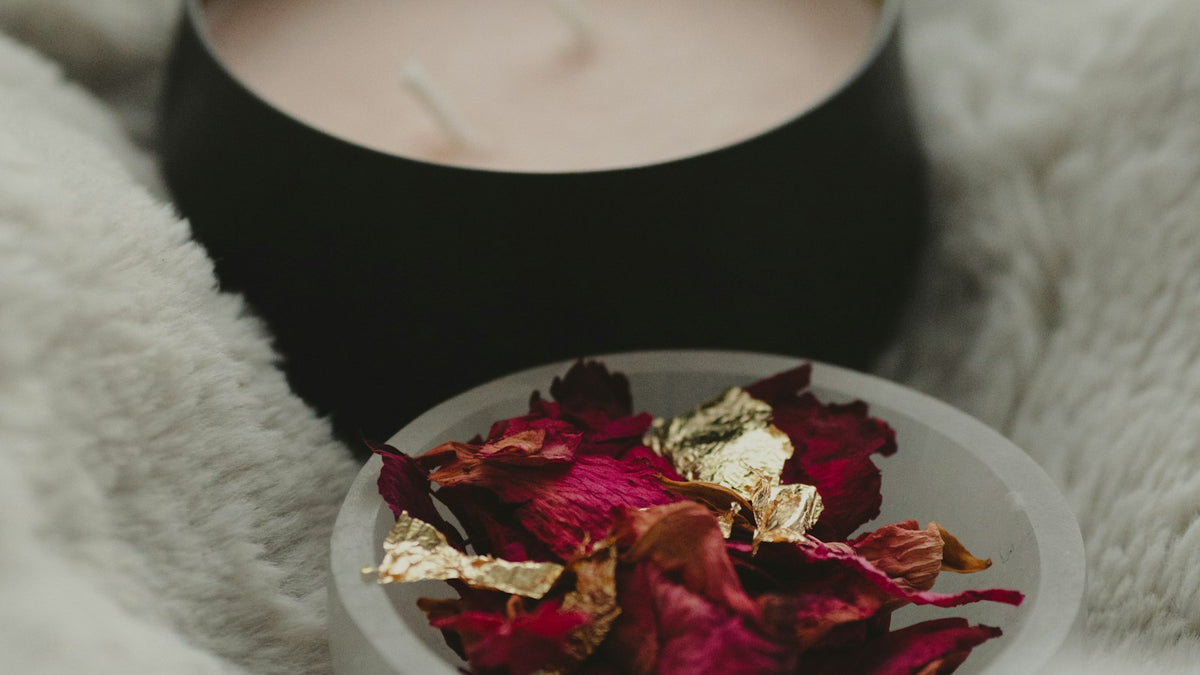 A candle beside a bowl of dried red rose petals