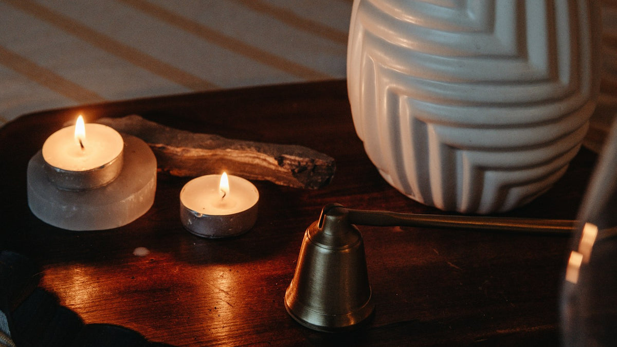 Two lit tea lights beside a brass candle snuffer on a wooden tray