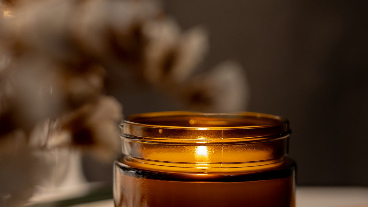 A lit candle in an amber glass jar