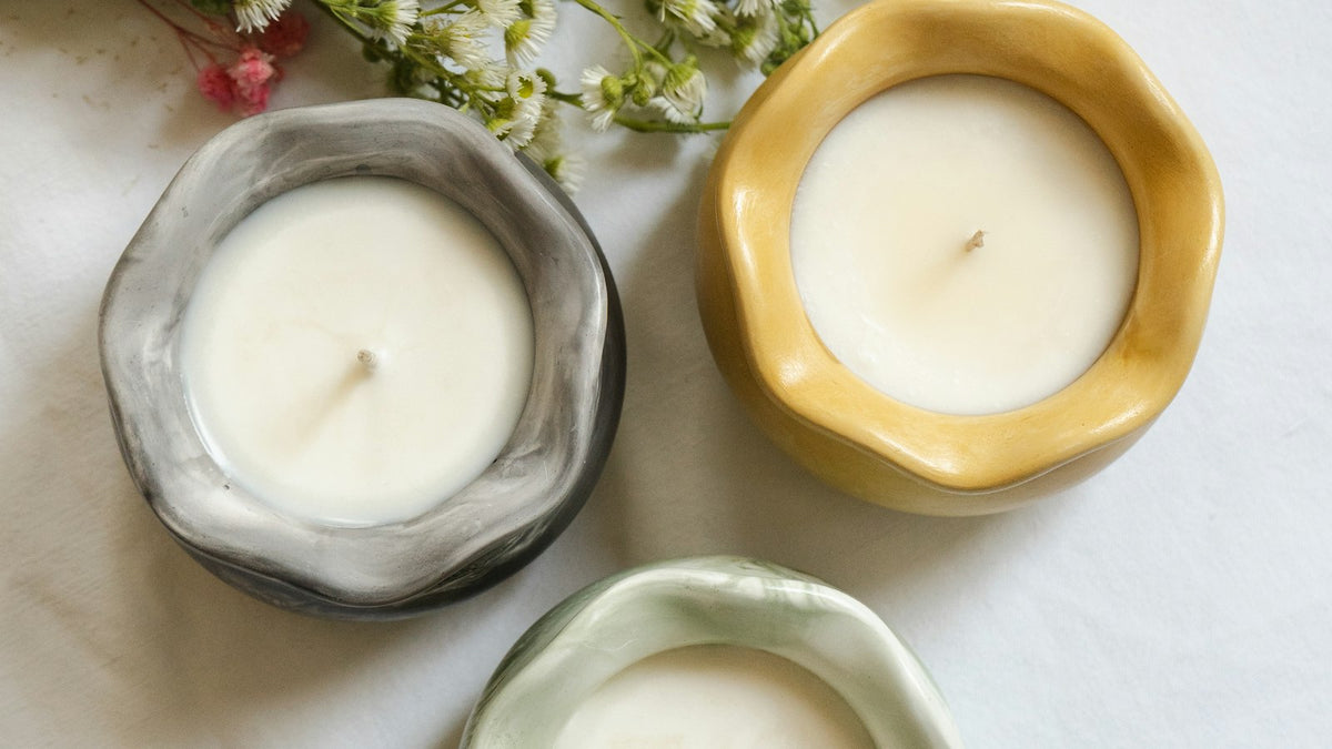 Three candles in ceramic vessels from above, with small white flowers