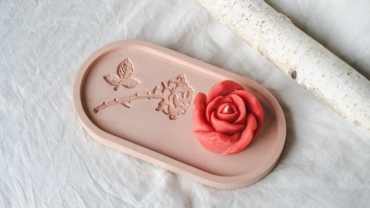 A red rose-shaped candle on a pink tray