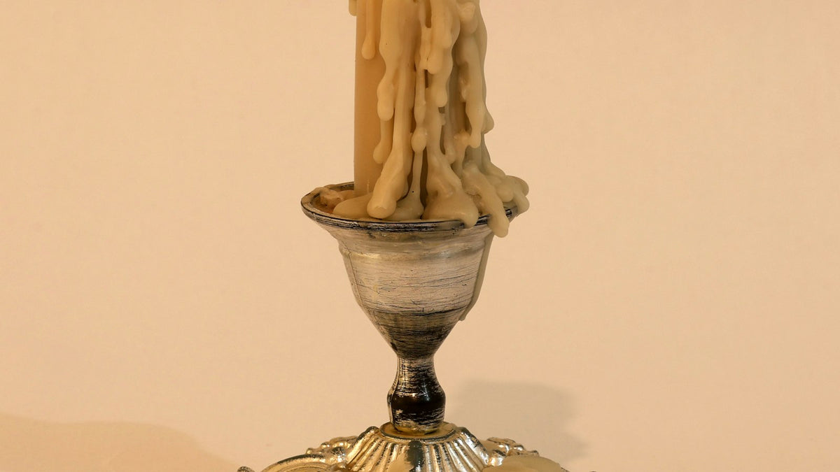 Wax drips down a taper candle onto a silver candle holder