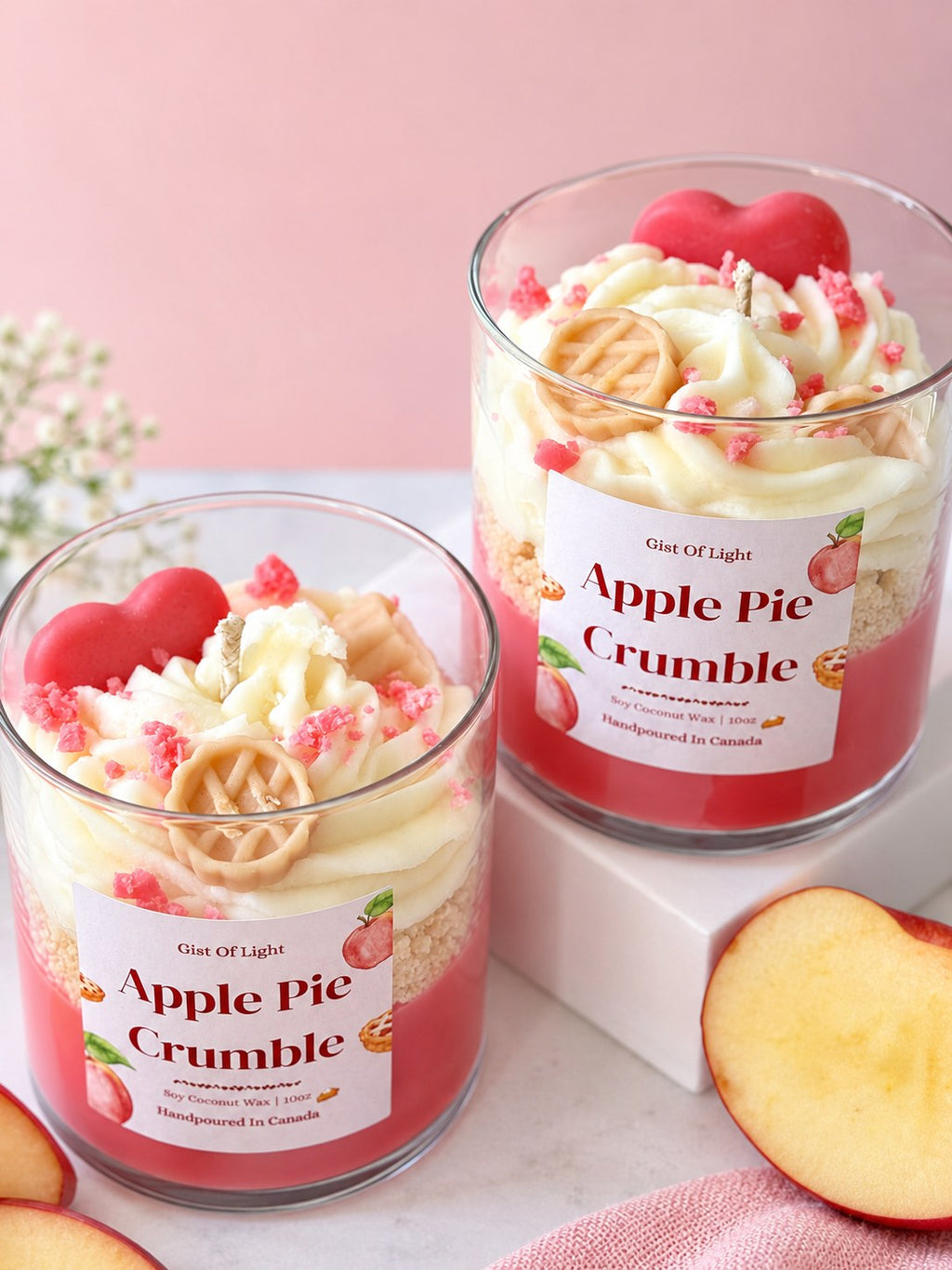 Two Apple Pie Crumble dessert candles with baby's breath and fresh apple halves on a pink backdrop