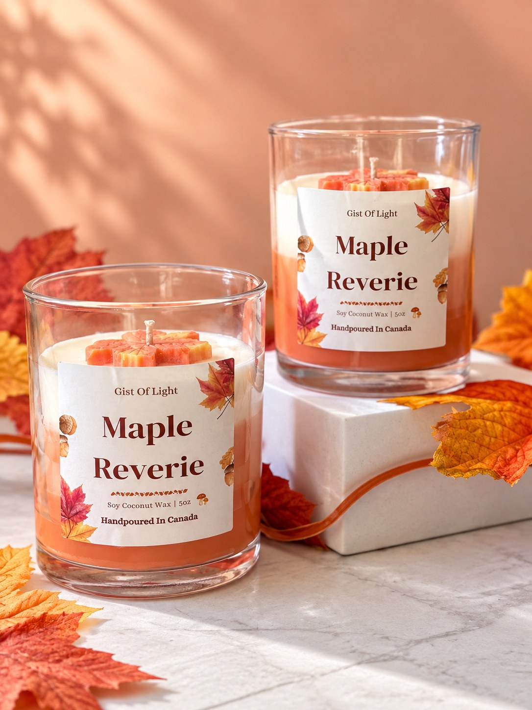 Two Maple Reverie fall candles in afternoon sunlight with orange autumn leaves