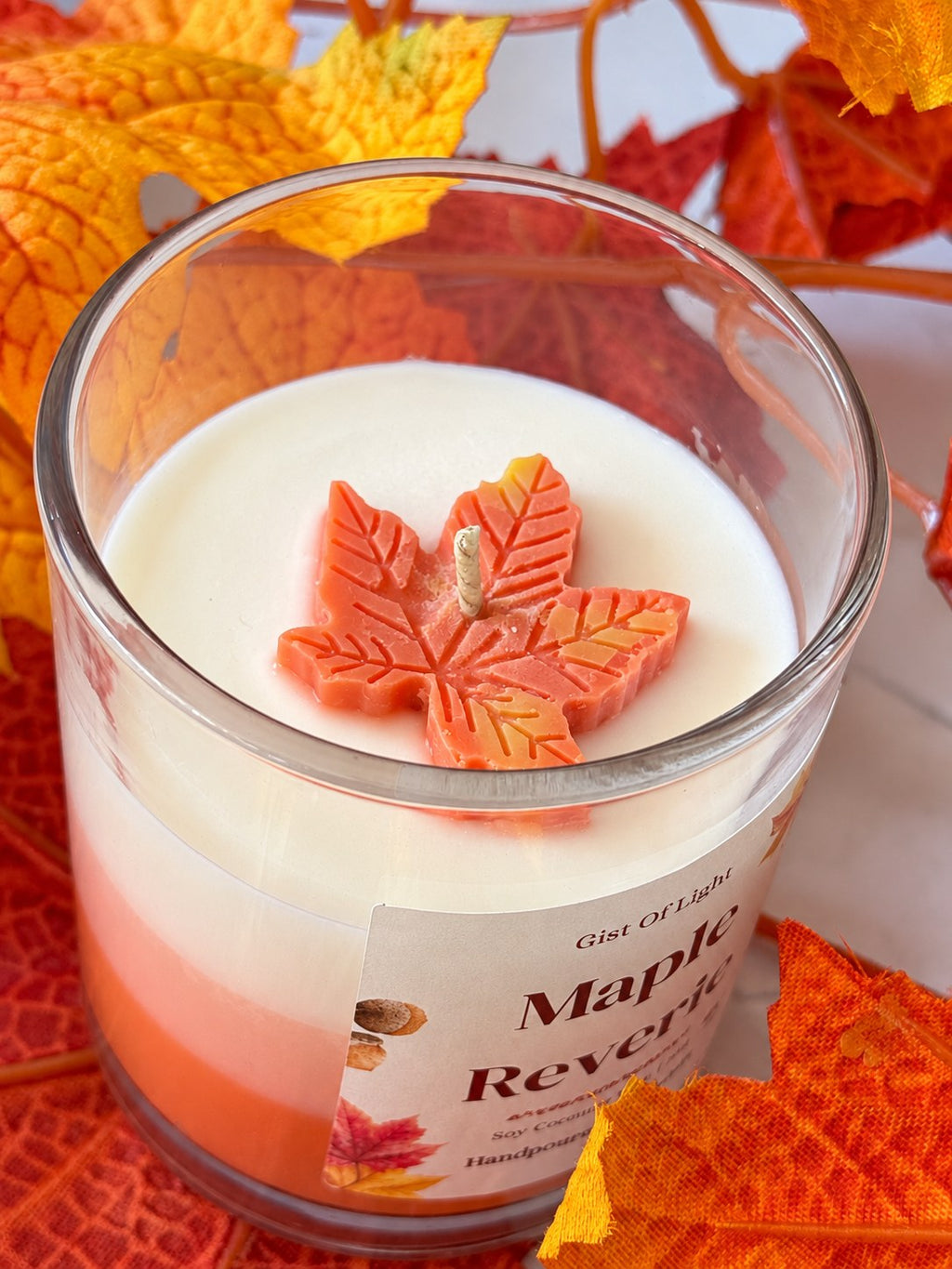 Close up of the Maple Reverie candle top with a moulded orange wax maple leaf and cotton wick