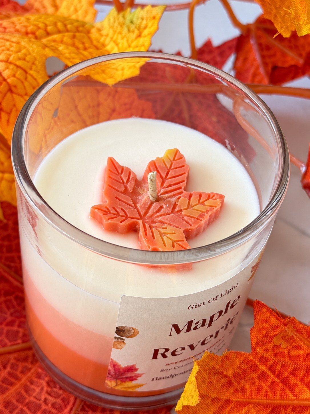 Close up of the Maple Reverie candle top with a moulded orange wax maple leaf and cotton wick