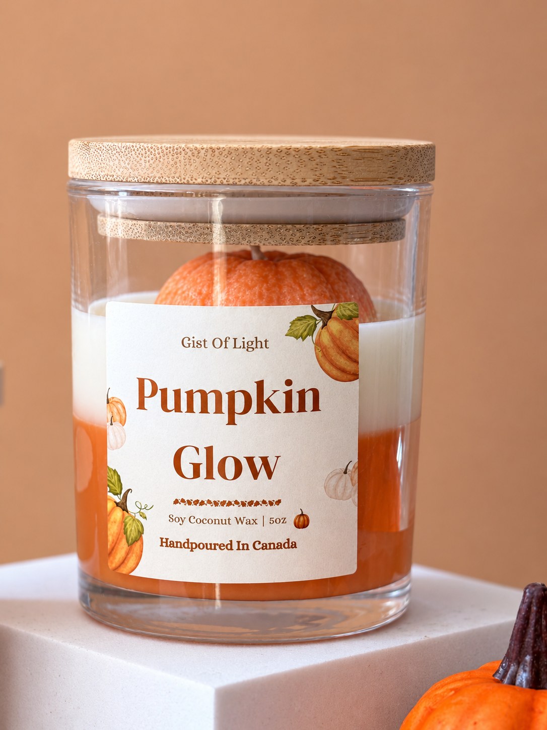 Pumpkin Glow 5 oz candle on a white plinth beside a small decorative pumpkin