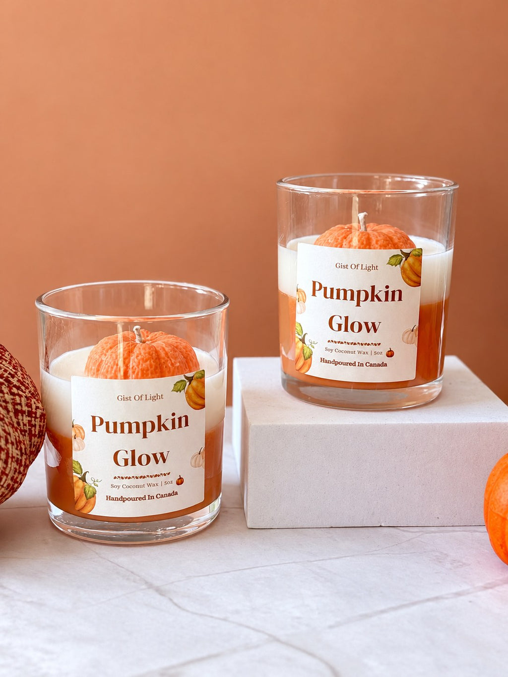 Two Pumpkin Glow fall candles on marble with small autumn pumpkins