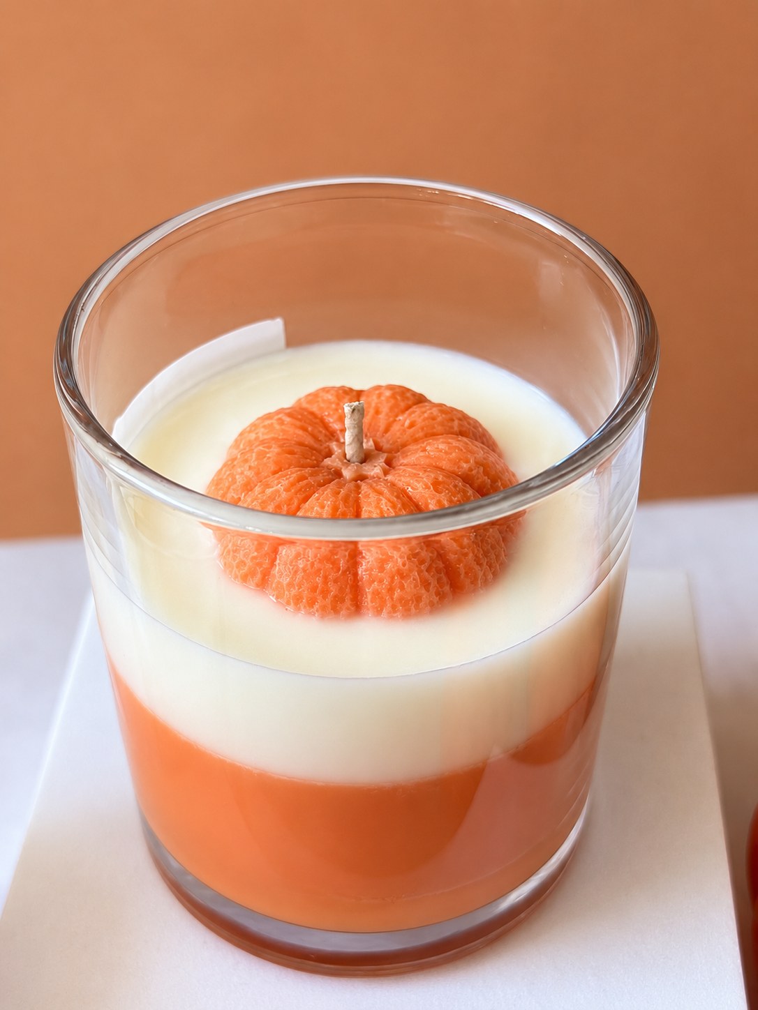 Close up of the Pumpkin Glow candle top with a moulded orange wax pumpkin around the cotton wick