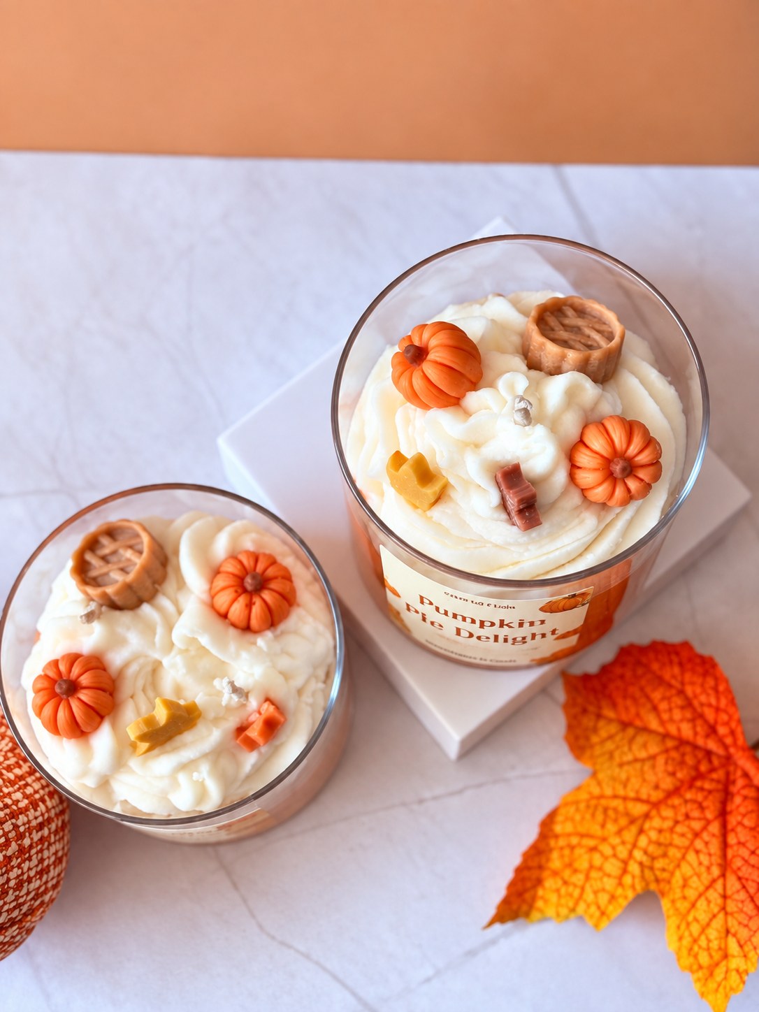 Two Pumpkin Pie Delight candles from above with wax pumpkins, a wax lattice pie and wax leaves