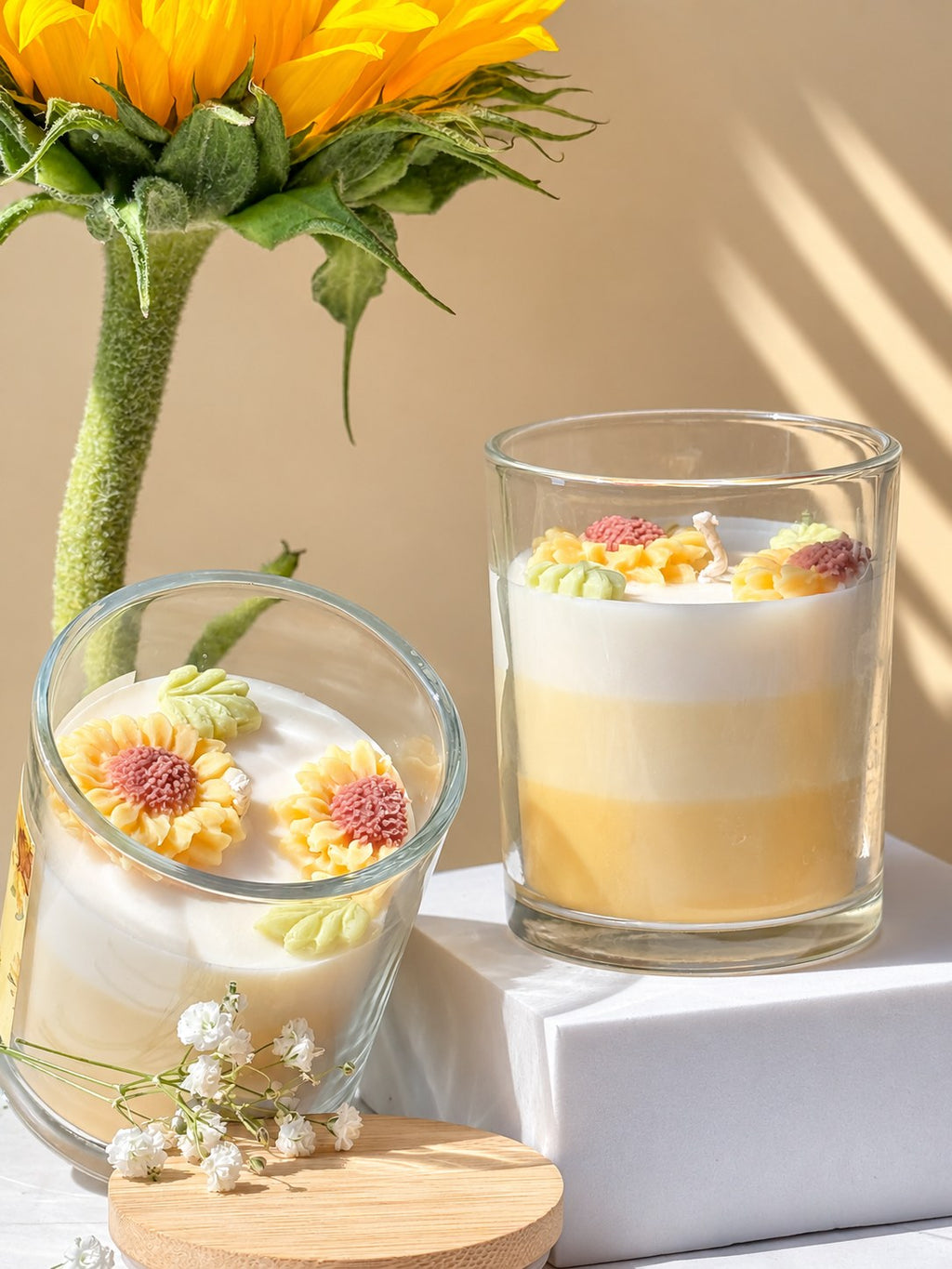 Two Sunny Hope candles in sunlight beside a fresh sunflower, showing the yellow and white wax layers