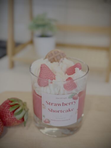 Decorative candle in a glass with strawberry shortcake design and real strawberries.